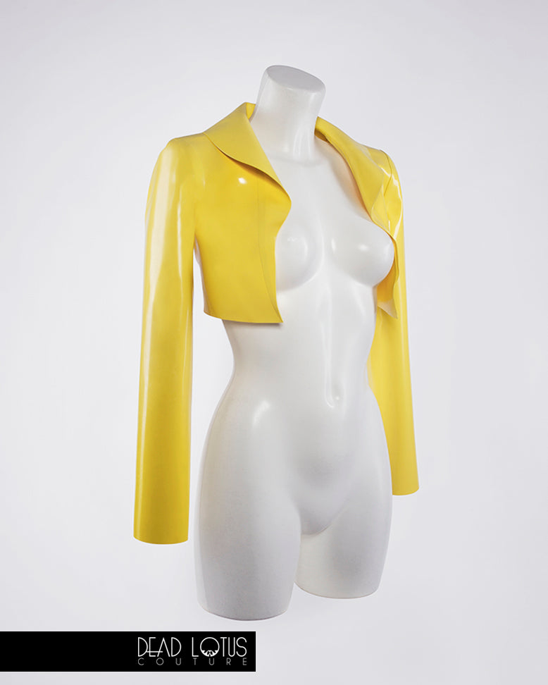 Yellow latex PLUVIA Bolero Jacket worn by model with collar up, a mini dress, corset and wrist gloves by Dead Lotus Couture